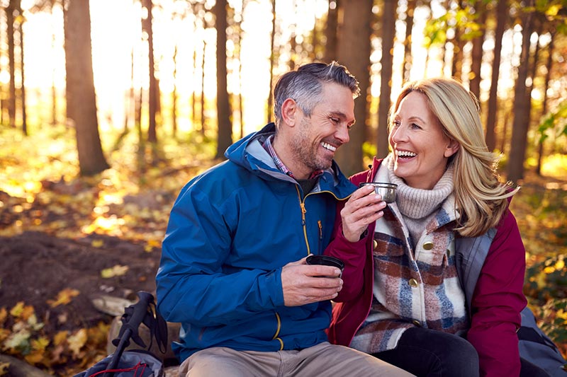 Older couple with perfect teeth enjoying a hot drink in a forest