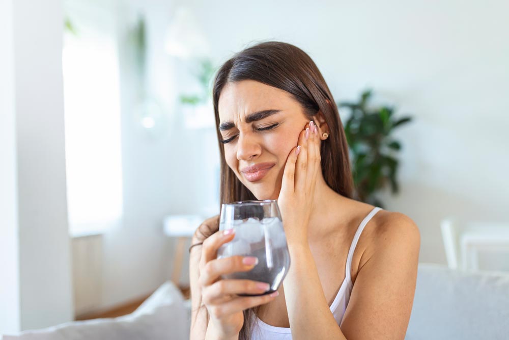 Woman showing tooth sensitivity and pain with a cold drink